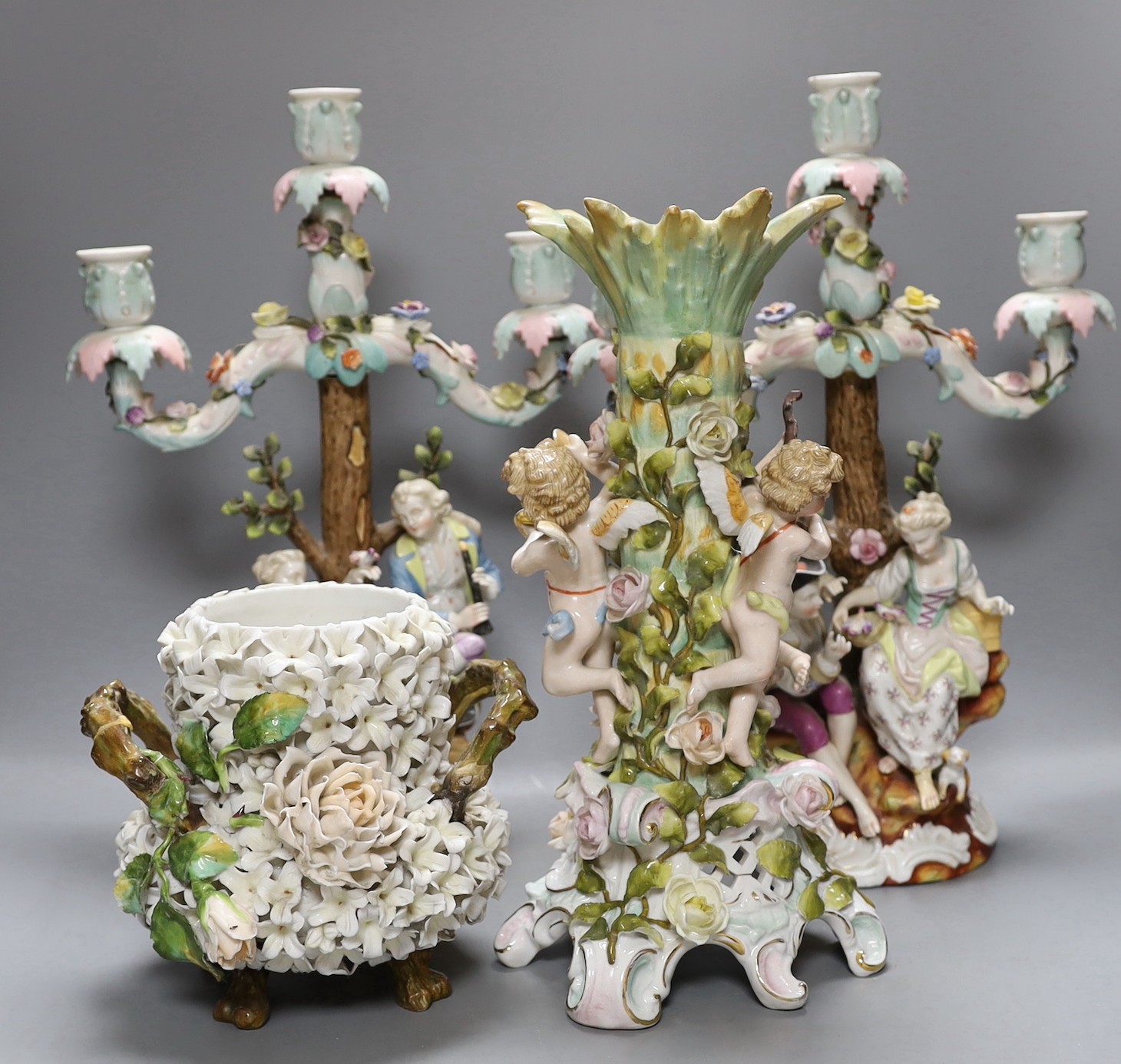 A pair of continental porcelain figural candlesticks and a similar candelabra base, together with a encrusted porcelain two handled jar with floral decoration, tallest 39cm, (4)